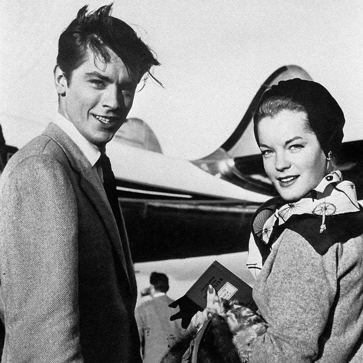 photo en noir et blanc de Romy Schneider portant le carré Hermès Les Bécanes datée du 21 mars 1959 en compagnie de Alain Delon sur le tarmac d'un aeroport