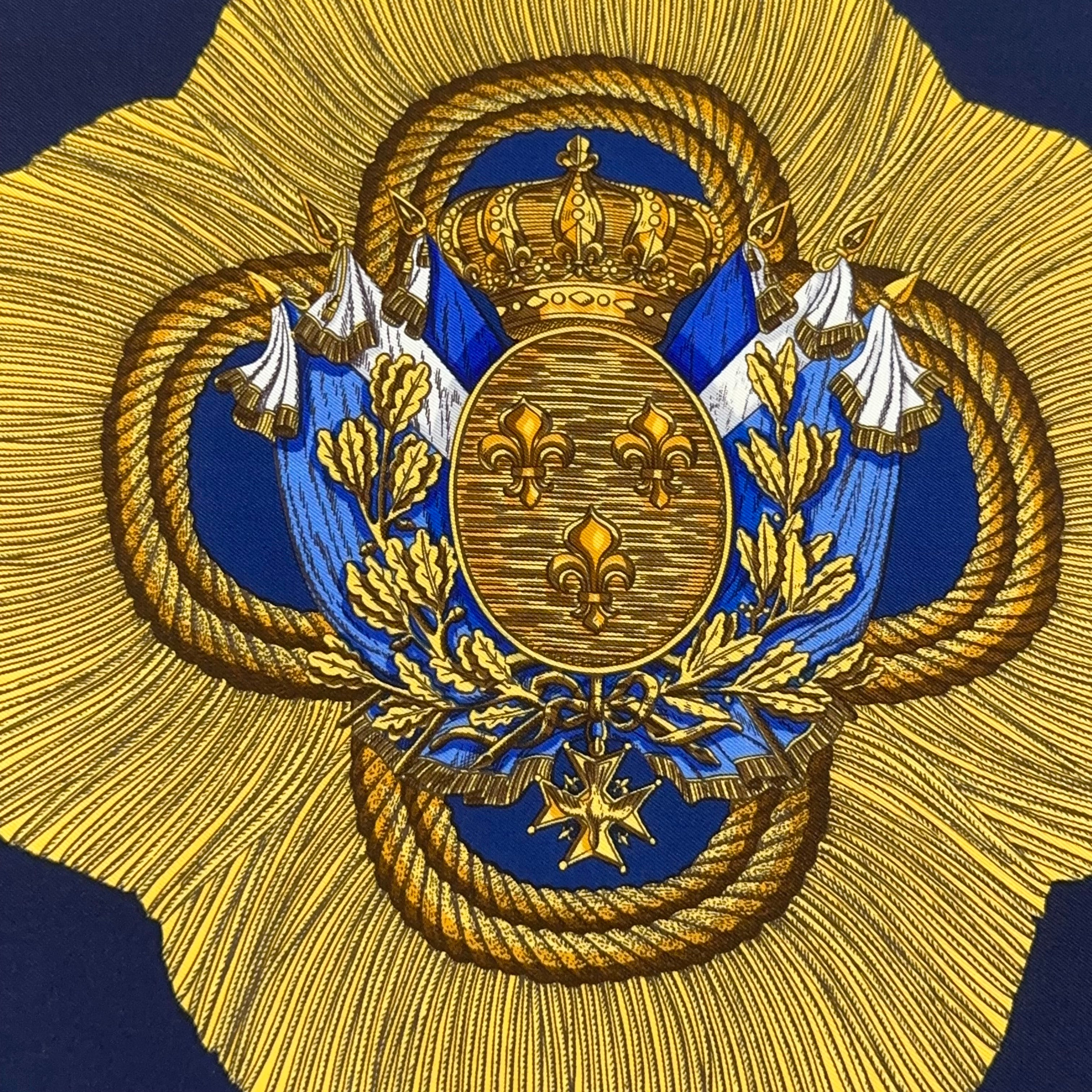Vue rapprochée du blason central : écu bleu à fleurs de lys d'or, couronne royale et drapeaux, détail de la finesse d'impression Hermès.