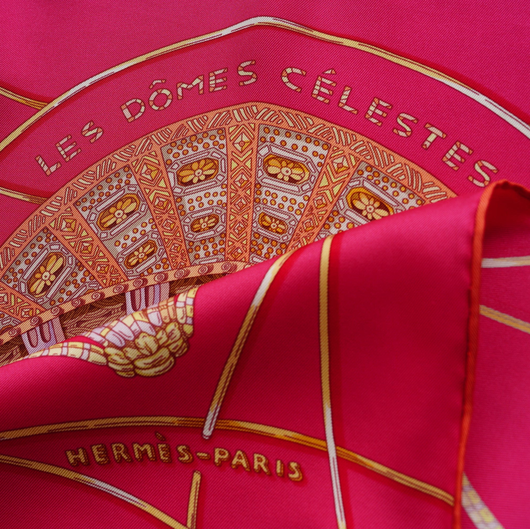 Gros plan sur l'angle du foulard montrant la bordure ocre et la signature "HERMÈS - PARIS", soulignant l'état impeccable des couleurs.