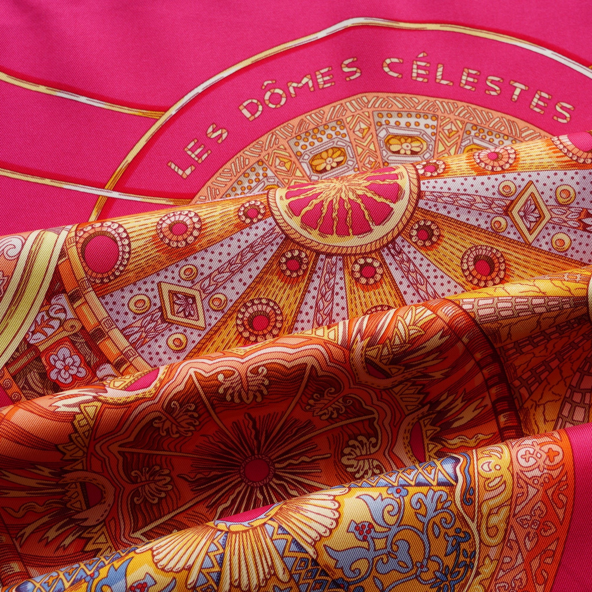 Gros plan sur le coin supérieur droit du carré Hermès, montrant le titre "LES DÔMES CÉLESTES" et le drapé soyeux de la soie vintage rose.