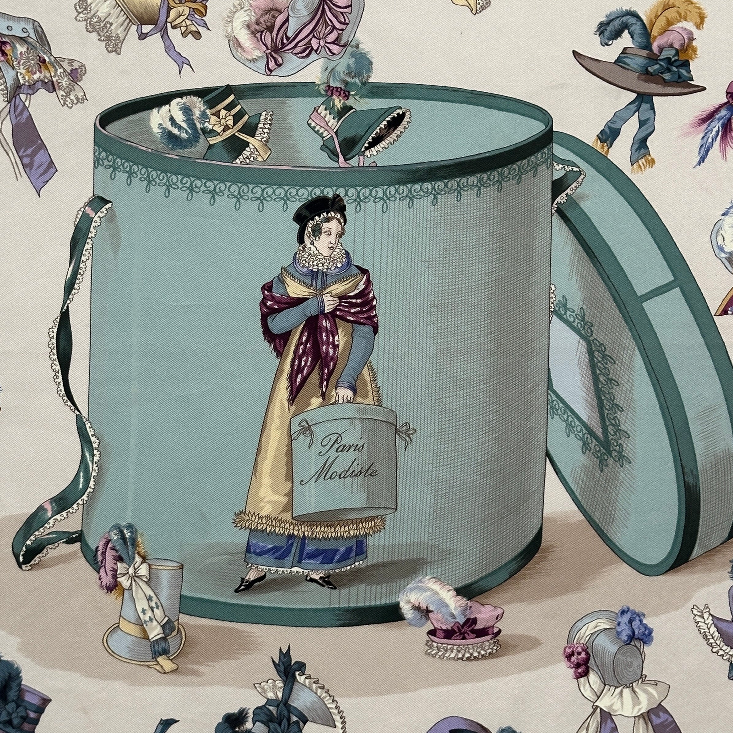 Gros plan sur le motif central du carré : une modiste parisienne se tenant devant une grande boîte à chapeaux bleue, entourée d'une envolée de coiffes anciennes.